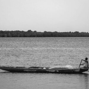 A serene black and white image of a child paddling a canoe on Cameroon's coastline.