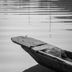 Serene black and white image of a wooden boat on tranquil water, capturing a peaceful and reflective mood.